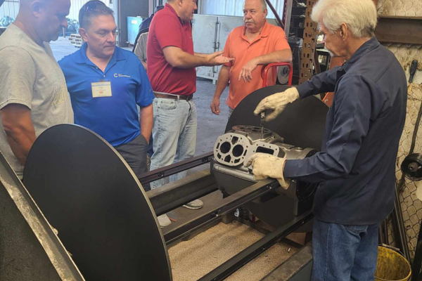 Group of technicians observing the remanufacturing process of a commercial HVAC compressor, with a focus on a compressor component being handled by an experienced worker.